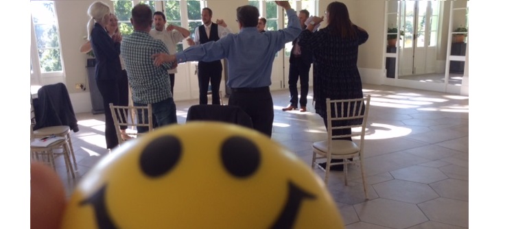 team of people doing laughter yoga, yellow smiley ball in foreground